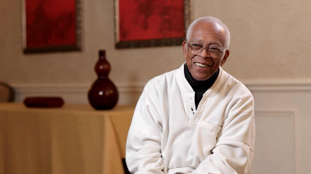 Black man with gray hair and glasses, seated and smiling warmly